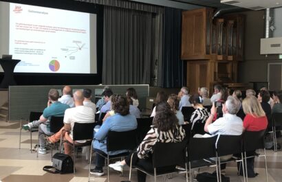 Presentatie bij Ipse de Bruggen met een groep mensen zittend op stoelen en kijkend naar een groot scherm