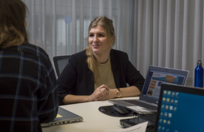 In een kantoorruimte zit een dame met een collega te praten met laptops op tafel