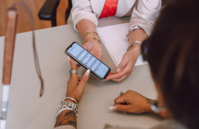 2 paar handen die een telefoon vasthouden waarop met grote letters tekst te lezen is